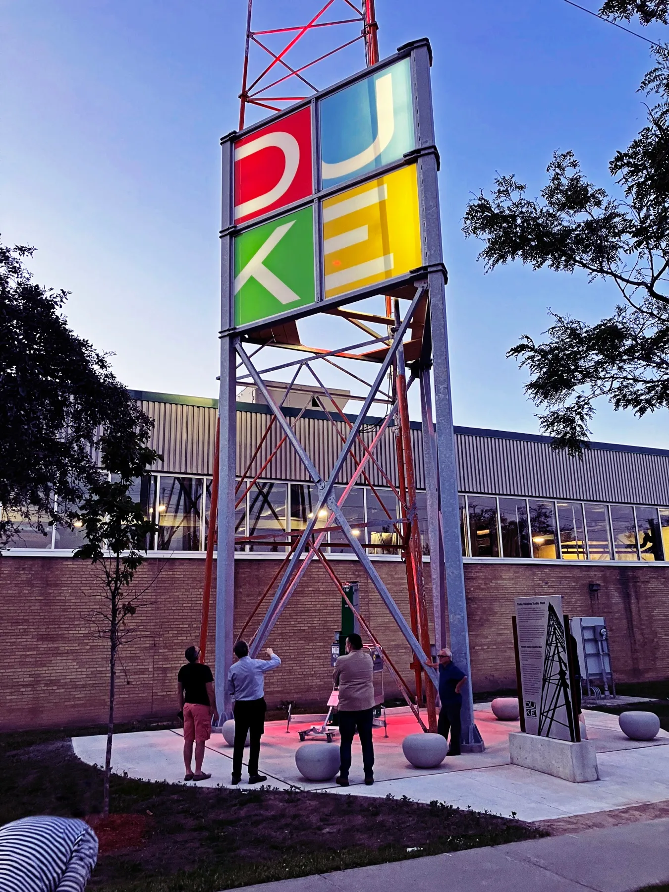 The Duke Heights BIA tower, an LED sign on a repurposed radio mast, with people at its base showing its scale